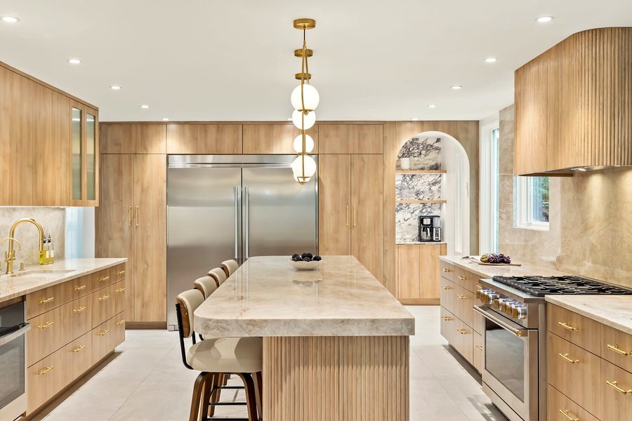 Oak kitchen with a quartzite island on a fluted oak base, globe pendants, a stainless fridge wall and a fluted oak hood