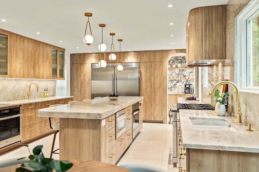Angled view of the oak kitchen with quartzite counters, brass fixtures, pendants and an arched marble niche