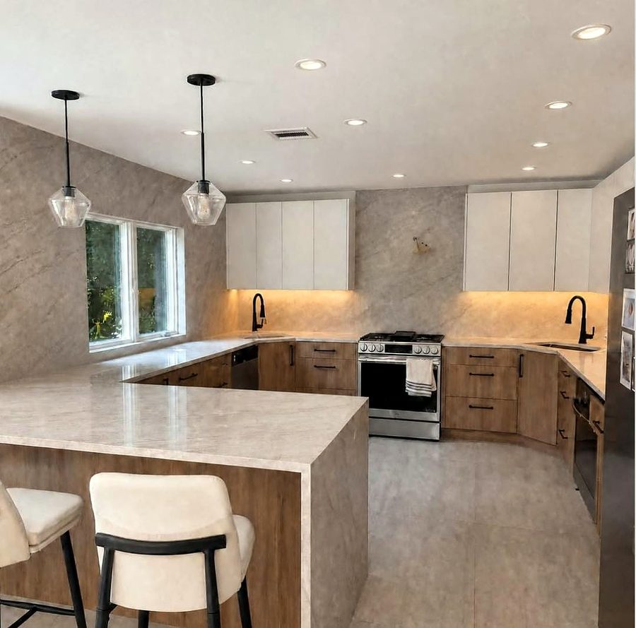U-shaped kitchen with a quartzite waterfall peninsula, oak lower cabinets, white flat-panel uppers and glass pendants